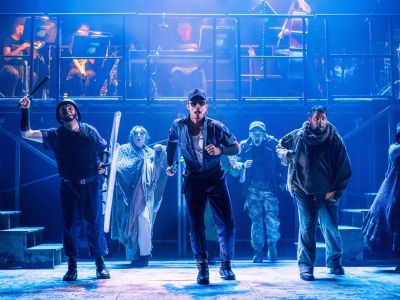 Actors dancing under a strong blue light on the set of Urinetown